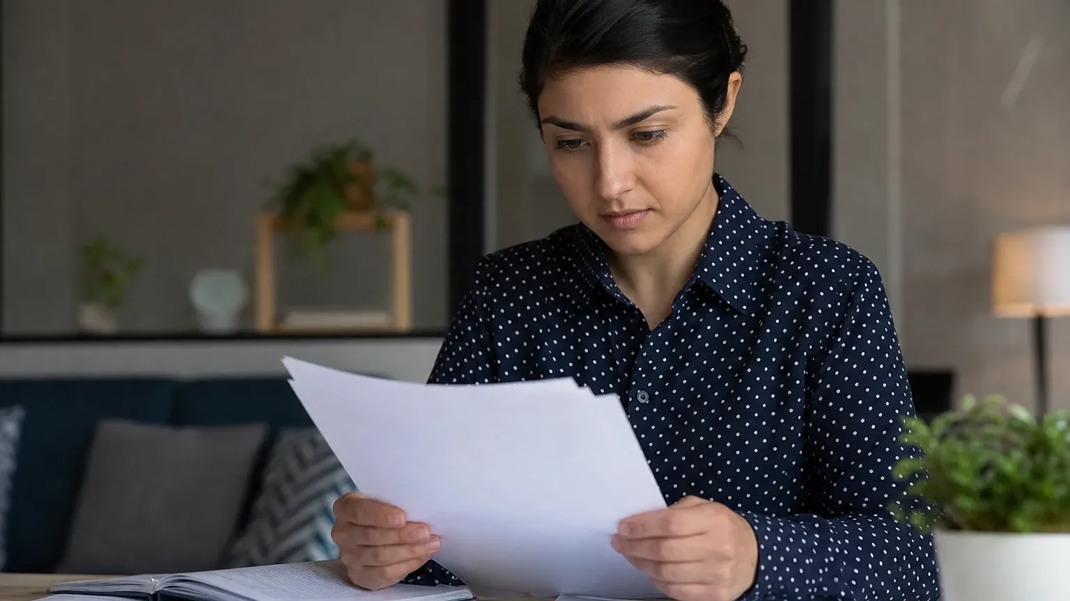 A person in a polka-dot shirt sits at a desk, reading papers, with an open notebook in front of them.
