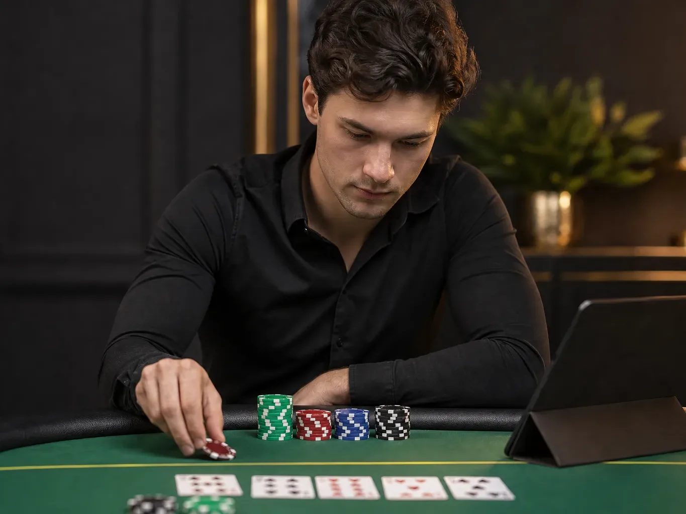 A person in a black shirt reaching for poker chips on a green felt table with playing cards laid out.