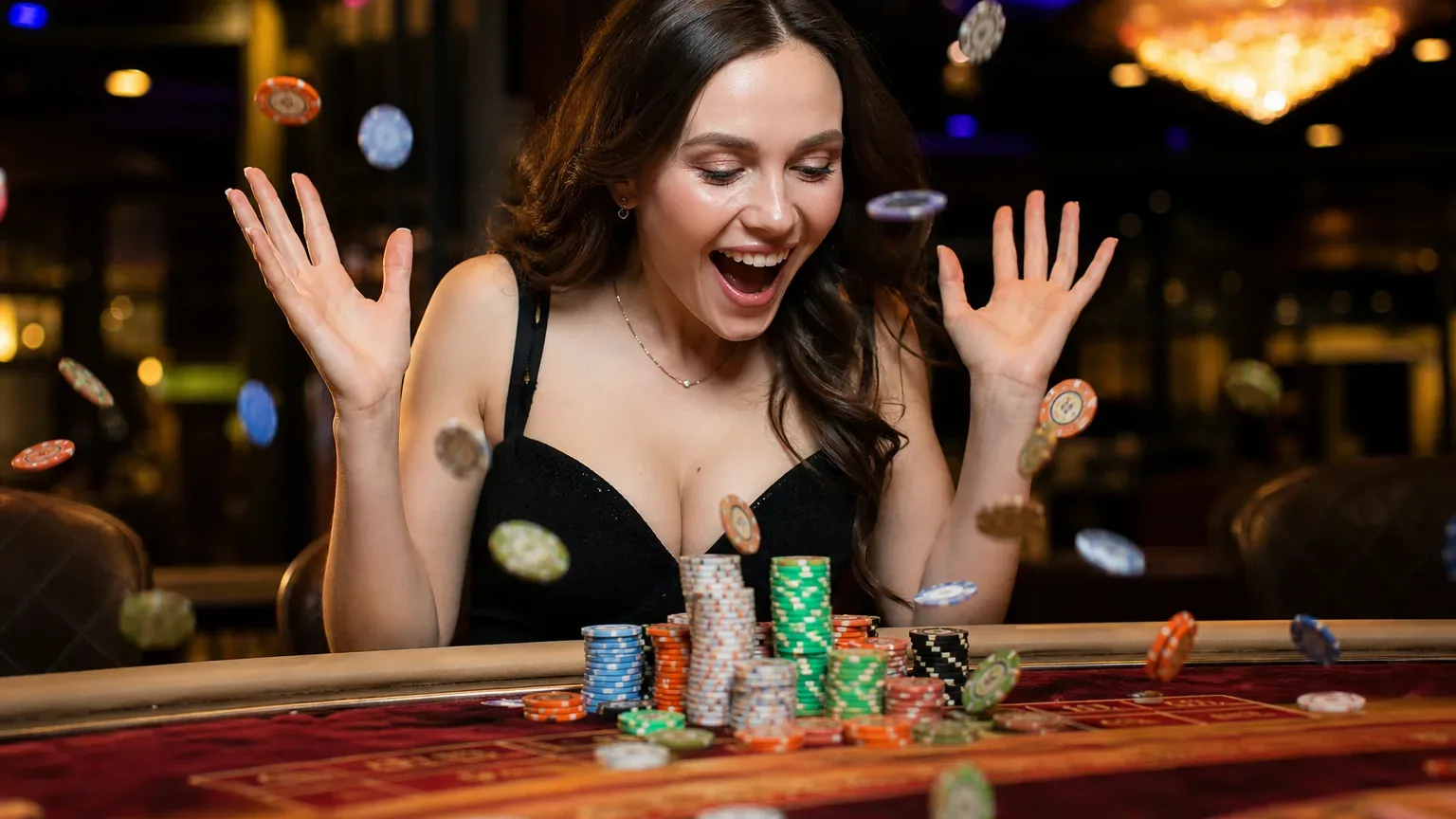 A person laughing and throwing casino chips into the air at a gaming table stacked with colourful chips.